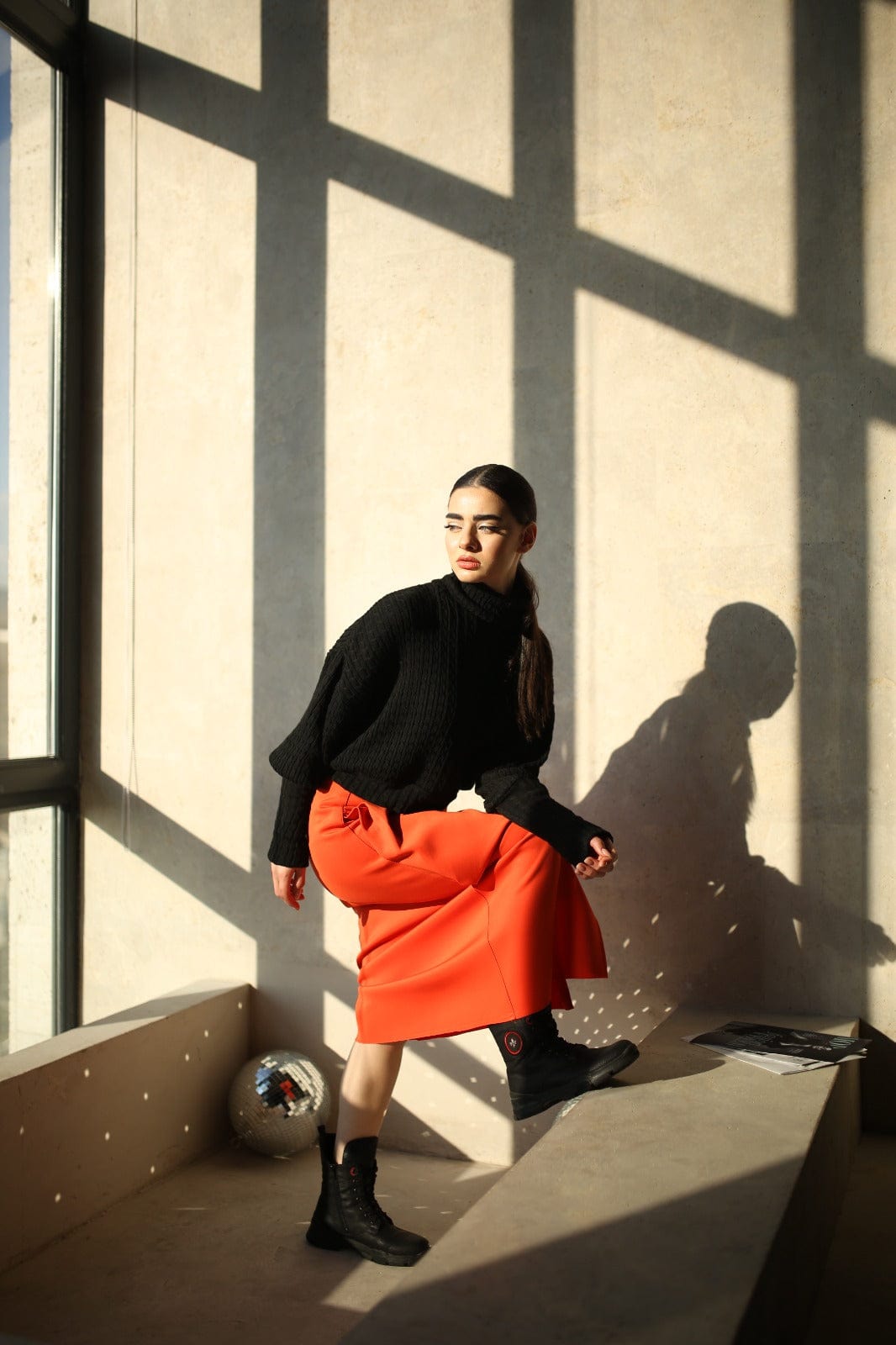 Woman in an orange cotton maxi skirt and black sweater in window light - Baleni
