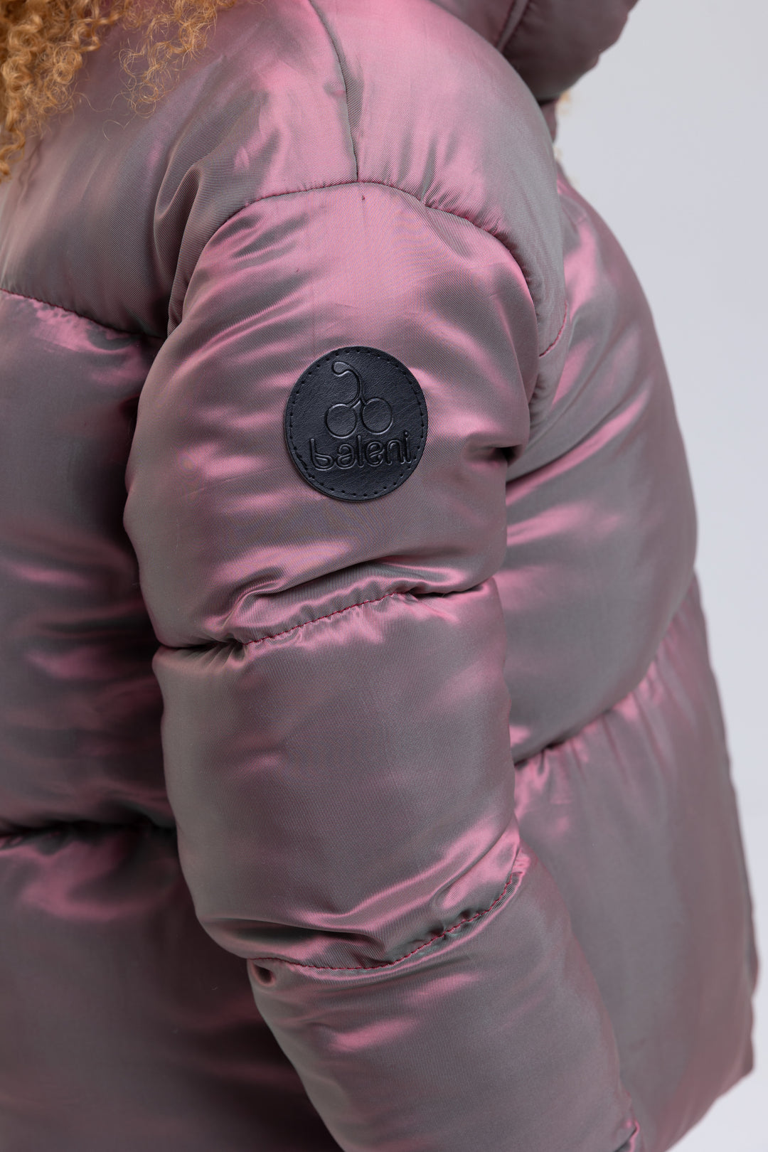 Close-up of the embossed leather logo patch on the sleeve of a pink puffer jacket - Baleni
