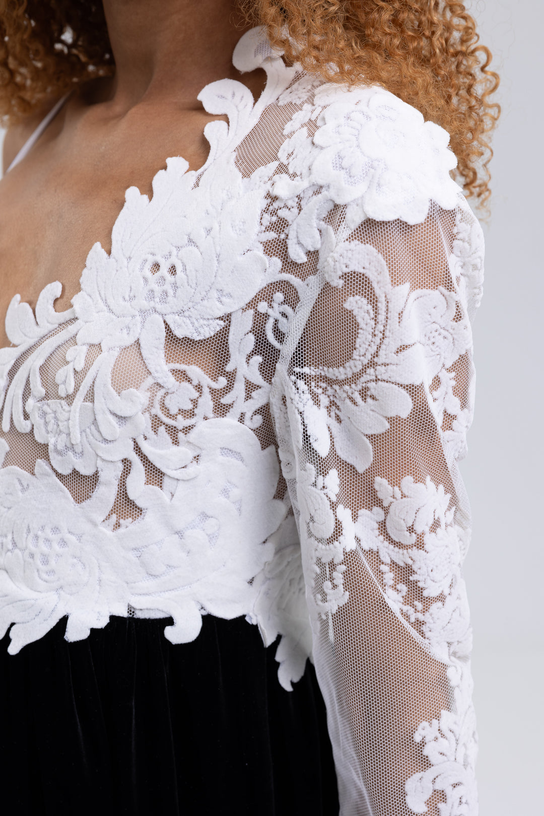 Close-up of the white floral lace bodice and sheer sleeve of a black and white evening gown - Baleni